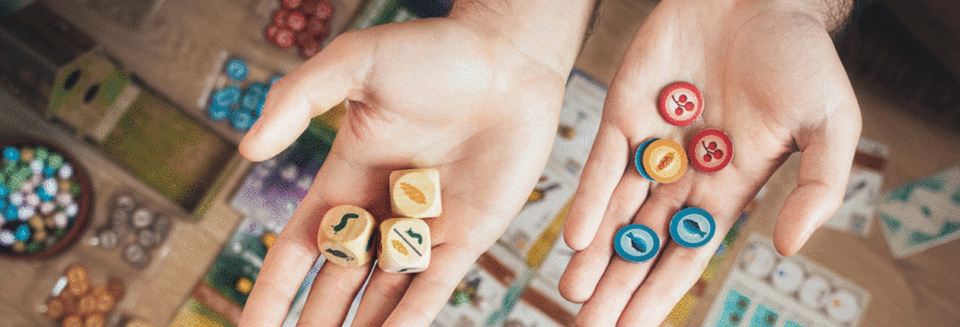 des mains tiennent des dès sur une table devant un jeu de société